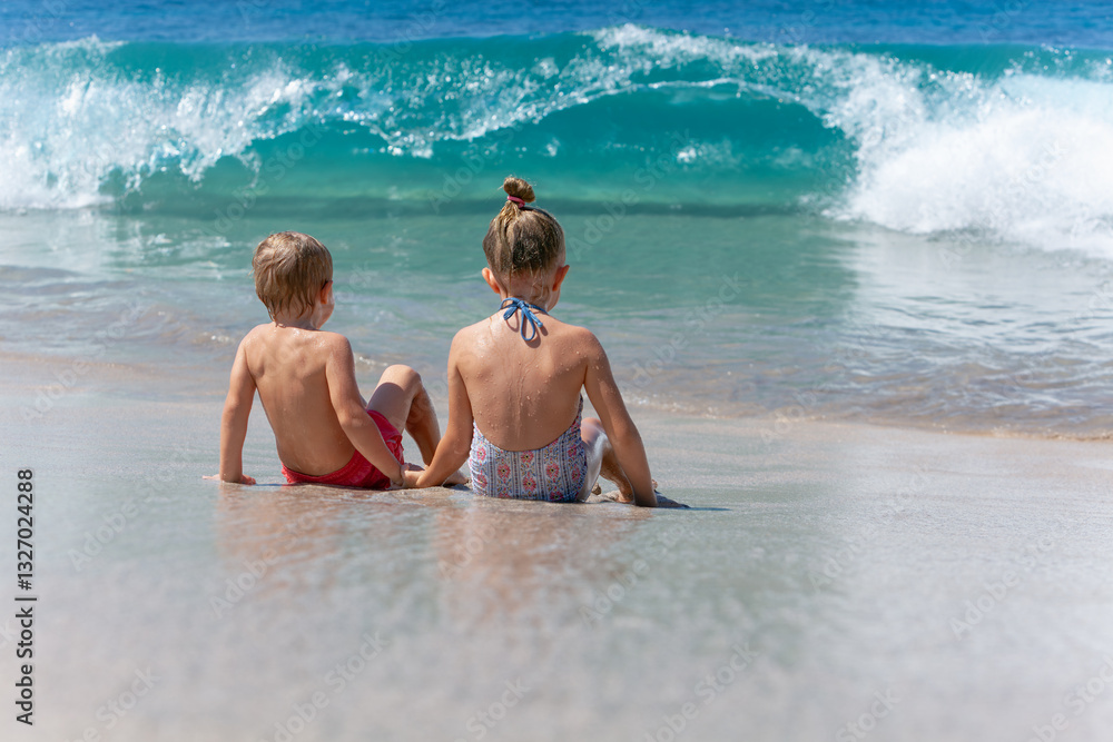Fototapeta premium Happy kids have fun in sea surf on white sand beach. Couple of children sit in water. Travel lifestyle, swimming activities in family summer camp. Vacations on tropical island.