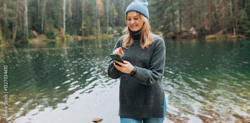 Obraz na płótnie Phone Communication. Check social networks. 30s Traveler woman in hat standing with phone near the majestic lake. Travel, adventure. Concept of an active lifestyle. w salonie