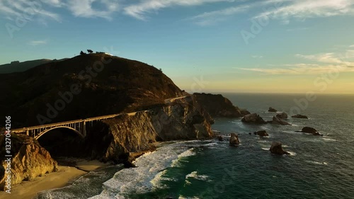 Aerial view of Bixby Creek Bridge at sunset with rugged cliffs and waves, Big Sur, California, United States.
