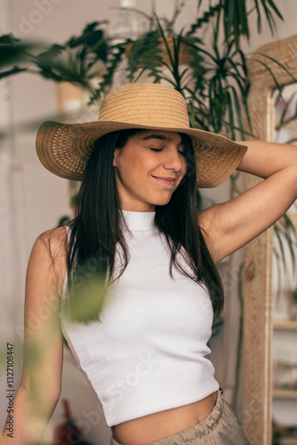 Portrait of a happy young dark-haired woman in a straw hat in a room with indoor plants.Summer concept.