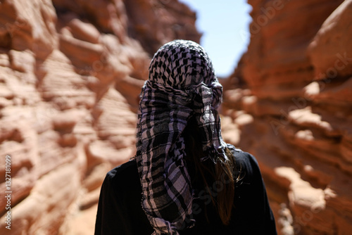 A person in a checkered scarf is in a narrow red canyon.
