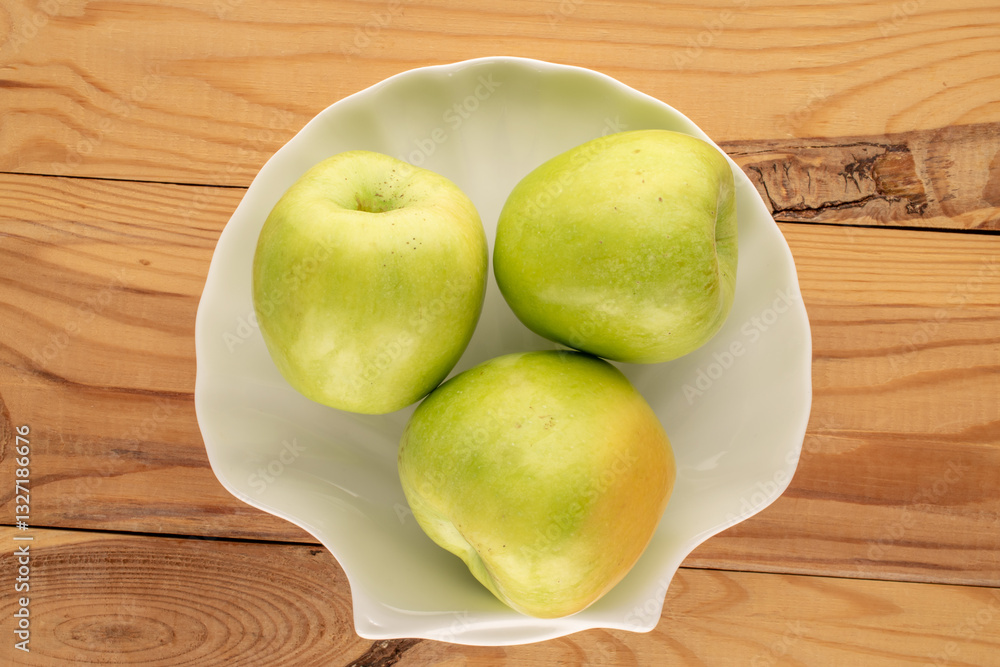 Several sweet green apples in a ceramic plate on a wooden table, close-up, top view. Several sweet green apples in a ceramic plate on a wooden table, close-up, top view.