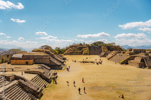 Tourists exploring Monte Alban, the ancient Zapotec archaeological site in Oaxaca, Mexico, under a clear blue sky.