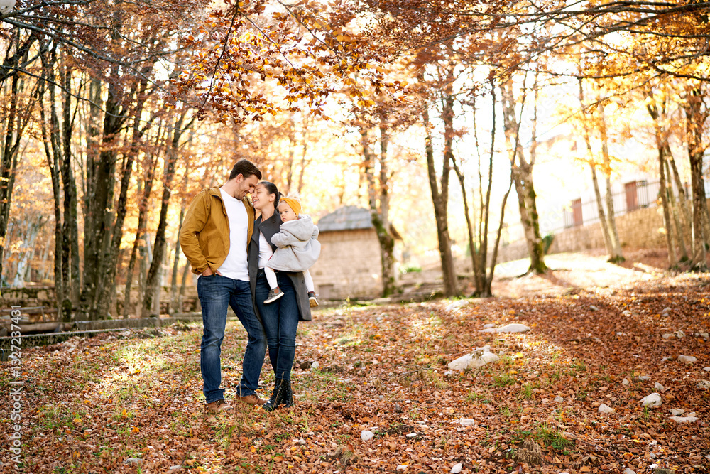 Dad touches his forehead with mom holding a little girl in her arms in the autumn forest Dad touches his forehead with mom holding a little girl in her arms in the autumn forest