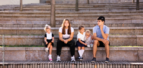 Children of different ages in school uniforms sitting on the steps outside