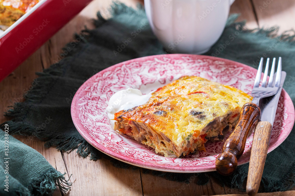 Oven baked omelette with vegetables served with sour cream on wooden background.