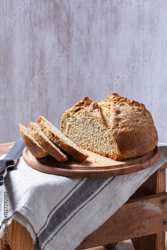 Homemade Irish soda bread cut into pieces and knife on wooden background.