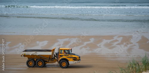 A dump truck carries loads of sand along the biscarosse dune coastline. The vehicle works to combat erosion as it traverses the wet, reflective sands near the ocean.
