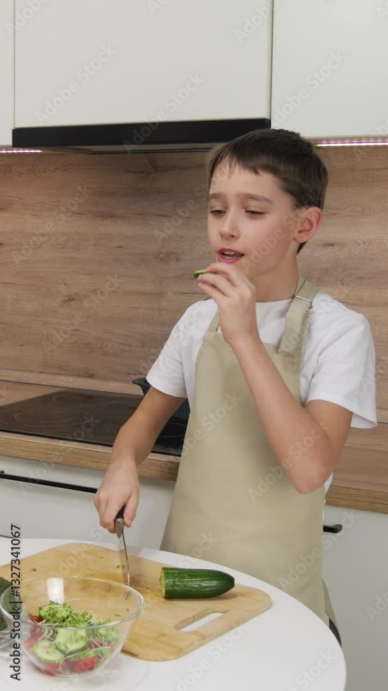 vertical screen. happy child preparing organic vegetable salad. child eating fresh vegetables while preparing salad. boy in apron enjoying taste of natural and nutritious vegetables