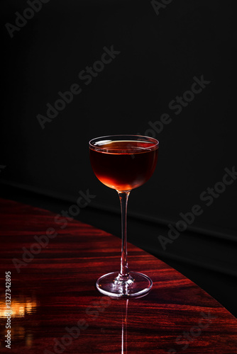A manhattan cocktail in a coupe glass on glossy wooden table in a bar with copy space