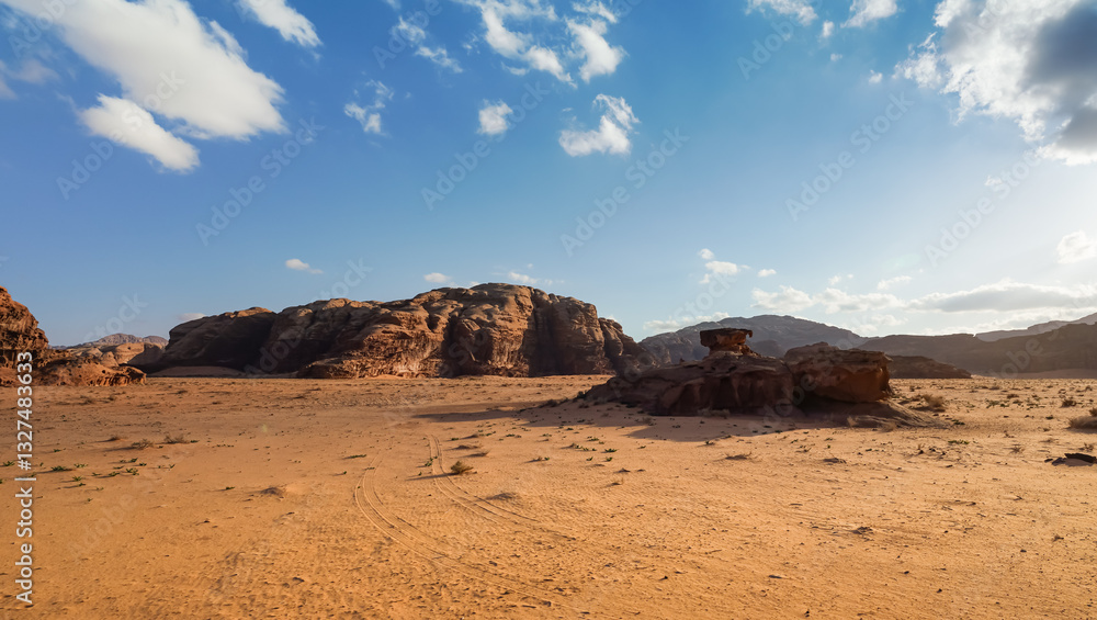Orange red sand desert, rocky formations and mountains background, blue sky above - typical scenery in Wadi Rum, Jordan