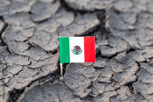 Flag of Mexico on dry cracked soil. Concept of drought in Mexico, rainless season, lack of water
