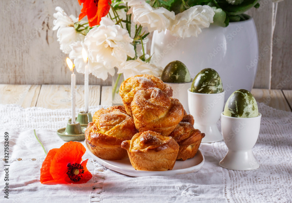 Easter still life of sweet buns, painted eggs and a bouquet of flowers on a light background.
