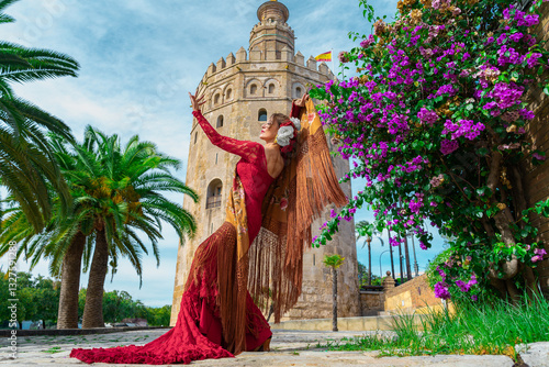 Mujer típica española bailando flamenco con una torre medieval y el cielo a su espalda. Desde la ciudad de Sevilla, Andalucía, España, Europa.	