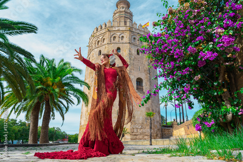 Mujer típica española bailando flamenco con una torre medieval y el cielo a su espalda. Desde la ciudad de Sevilla, Andalucía, España, Europa.	