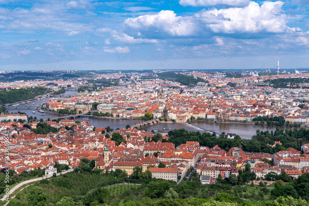 Obraz premium Panoramic view of Prague with the Vltava River, historic bridges, and red rooftops, surrounded by lush greenery. Stunning European cityscape showcasing Czech Republic’s architectural and natural beaut