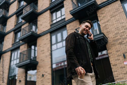 Wallpaper Mural Shooting from below of cheerful young man in casual clothes holding paper cup of coffee and talking on smartphone while walking down street by modern brick building. Concept of urban lifestyle. Torontodigital.ca