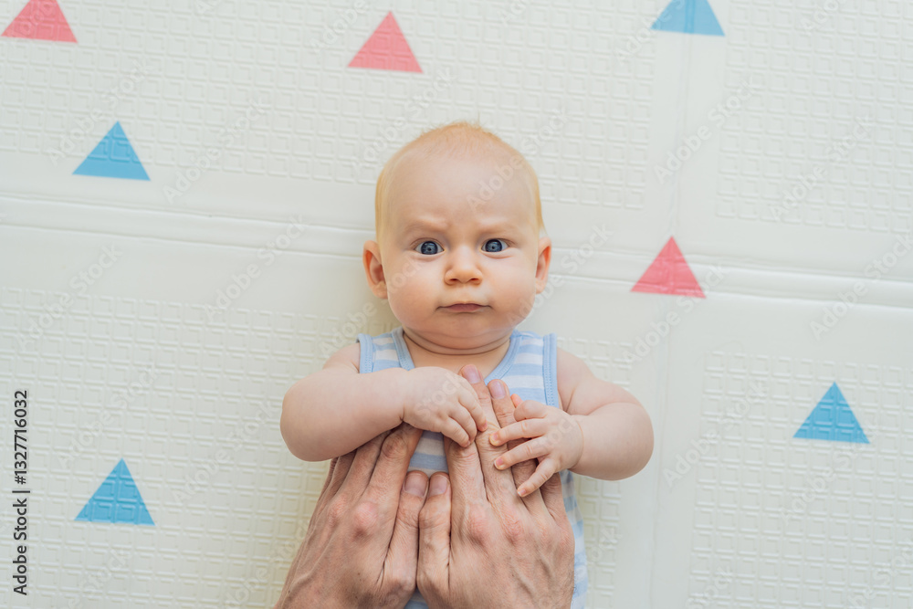 A baby lies on a soft children play mat while their father hands gently support and protect them. Heartwarming moment of care and connection. Parenthood, safety, and love concept