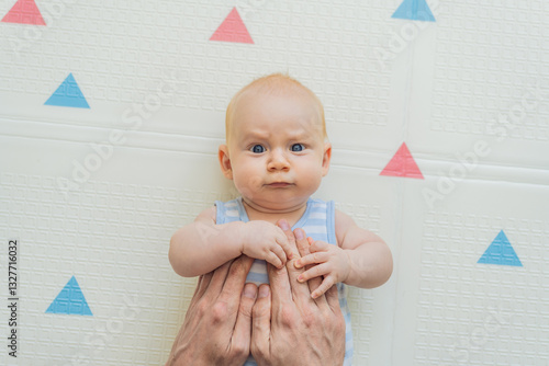 Obraz na płótnie A baby lies on a soft children play mat while their father hands gently support and protect them. Heartwarming moment of care and connection. Parenthood, safety, and love concept w salonie