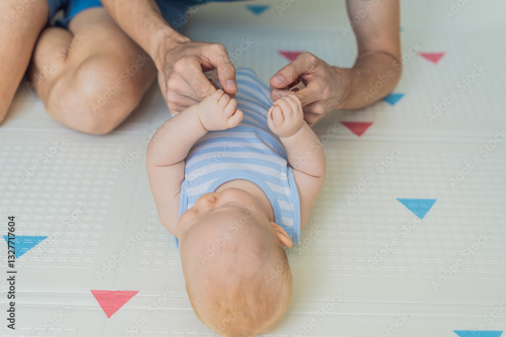 A baby lies on a soft children play mat while their father hands gently support and protect them. Heartwarming moment of care and connection. Parenthood, safety, and love concept
