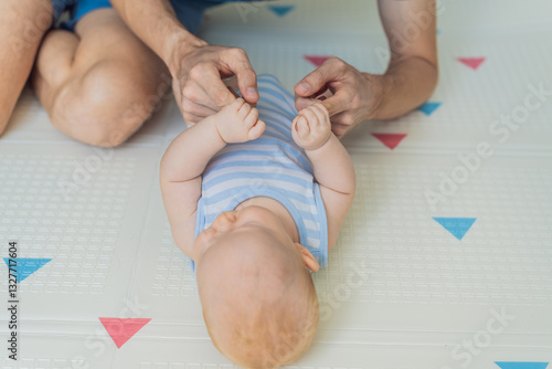 Obraz na płótnie A baby lies on a soft children play mat while their father hands gently support and protect them. Heartwarming moment of care and connection. Parenthood, safety, and love concept w salonie