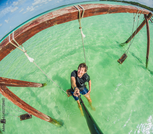 Male tourist enjoying a swing over the turquoise waters of Lake Bacalar, Mexico. A fun and adventurous experience in nature, capturing the essence of outdoor leisure and water exploration