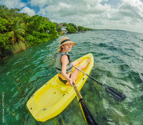 Unaltered woman tourist kayaking on the serene turquoise waters of Lake Bacalar, Mexico, surrounded by natural beauty. Adventure, relaxation, and outdoor travel concept in a peaceful tropical