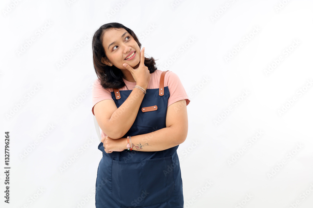 Asian woman wearing apron putting her hand on chin looking pensive imagining something on white background, empty space for advertising content Asian woman wearing apron putting her hand on chin looking pensive imagining something on white background, empty space for advertising content