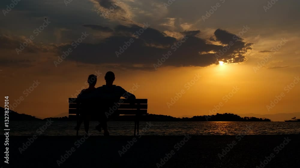 Silhouette of a man and woman on a bench. An embracing couple silhouette pass time together on the bay during evening holidays. Silhouette of a man and woman on a bench. An embracing couple silhouette pass time together on the bay during evening holidays.