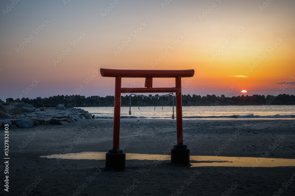 日の出を迎える海岸の鳥居と印象的な岩
