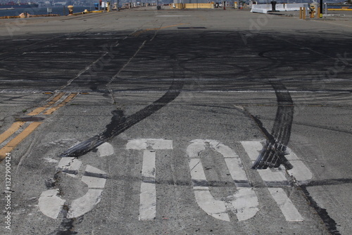 Obraz na płótnie Cracked asphalt road with a large white stop sign and tire skid marks at an urban intersection emphasizing traffic safety and road conditions w salonie