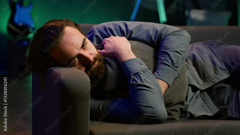 Man laying down hugging pillow watching TV, heartbroken by upsetting movie plot. Sad viewer lounged on couch in RGB illuminated apartment, upset by depressing television show scene, camera A Man laying down hugging pillow watching TV, heartbroken by upsetting movie plot. Sad viewer lounged on couch in RGB illuminated apartment, upset by depressing television show scene, camera A