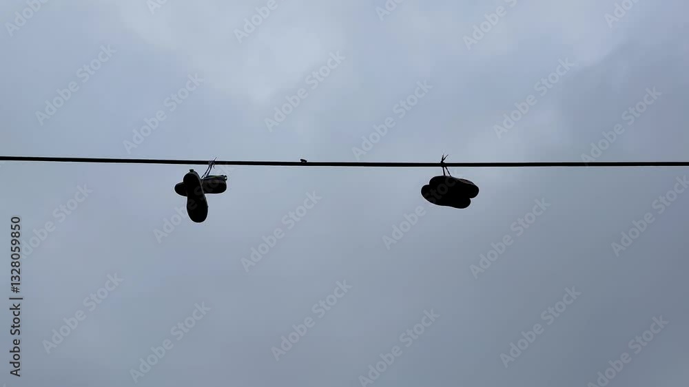 A unique pair of shoes hangs on a power line against a dramatic cloudy sky, capturing urban culture and community A unique pair of shoes hangs on a power line against a dramatic cloudy sky, capturing urban culture and community