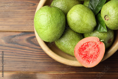 Fototapeta Naklejka Na Ścianę i Meble -  Fresh cut and whole guava fruits in bowl on wooden table, top view. Space for text