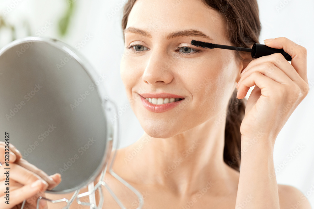 Smiling young woman looking at hand mirror, applying mascara, home interior, copy space. Cheerful attractive lady holding mirror, using mascara, getting ready before party, closeup Smiling young woman looking at hand mirror, applying mascara, home interior, copy space. Cheerful attractive lady holding mirror, using mascara, getting ready before party, closeup