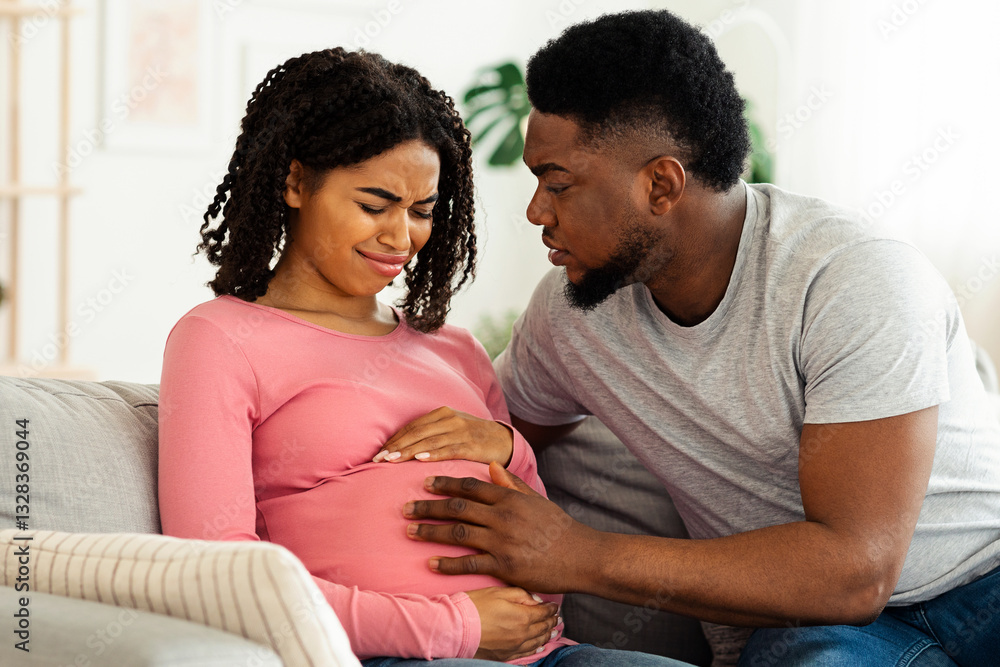 Fototapeta premium Attentive african husband supporting his pregnant wife in pain, home interior