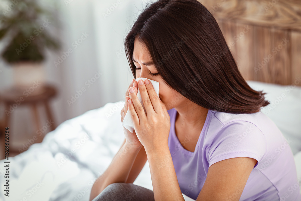 Sick At Home. Asian Girl Blowing Nose In Paper Tissue Having Rhinitis Symptom Sitting On Bed In Bedroom. Copy Space