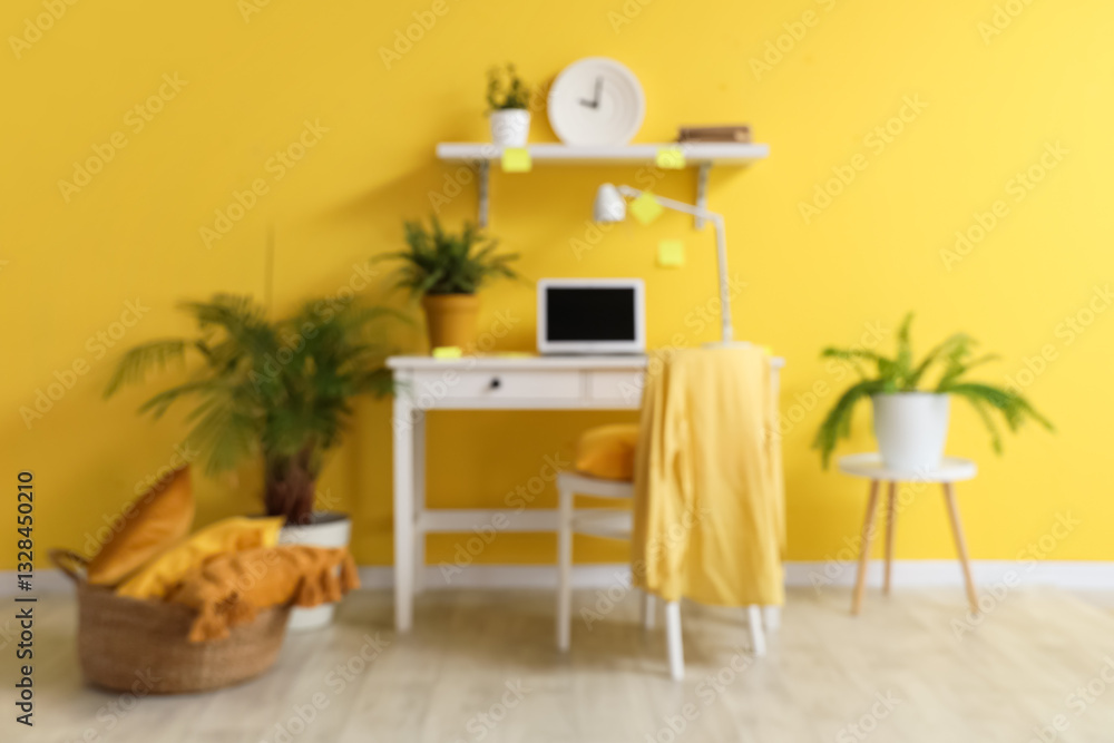 Fototapeta premium Stylish room with workplace, modern laptop, chair and clock on yellow wall, blurred view