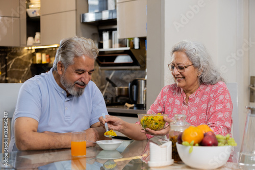 Happy retired senior indian couple eating healthy breakfast together, Elderly husband wife enjoy food at table, Love and bonding. Retirement life.