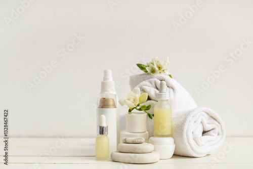 Composition with cosmetic products, spa stones, clean towels and flowers on light wooden table