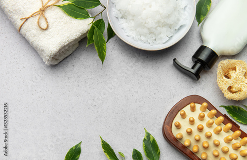 Wellness and spa composition with magnesium flakes, towel, massage brush, essential oil and green leaves on grey background