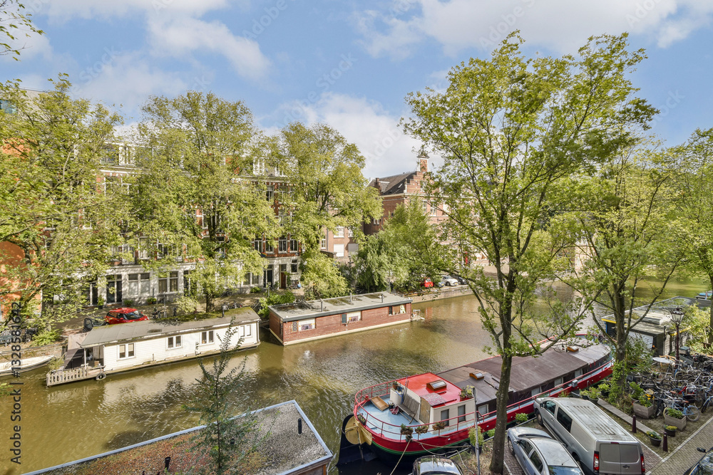 Fototapeta premium A picturesque canal scene showcases lush trees, residential buildings, and colorful boats along the waterway, ideal for relaxation and exploration.