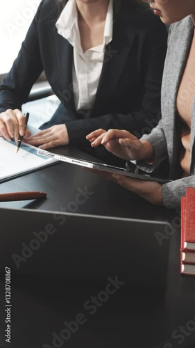 Two female lawyers in business suits meet at wooden desk, shaking hands over contract paper. wooden gavel and scales justice as discuss legal compliance, corporate law, dispute resolution.