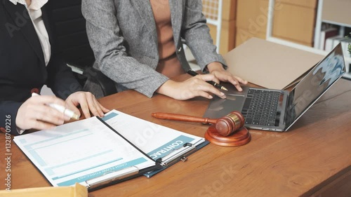 Two female lawyers in business suits meet at wooden desk, shaking hands over contract paper. wooden gavel and scales justice as discuss legal compliance, corporate law, dispute resolution.