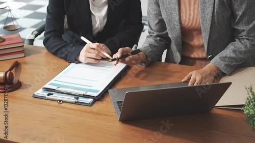 Two female lawyers in business suits meet at wooden desk, shaking hands over contract paper. wooden gavel and scales justice as discuss legal compliance, corporate law, dispute resolution.