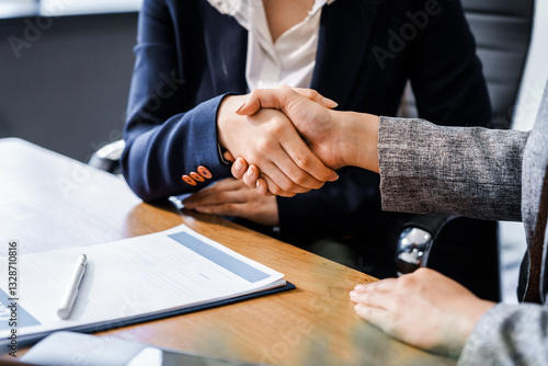 Two female lawyers in business suits shake hands at wooden desk, finalizing legal agreement. wooden gavel and scales represent justice as they discuss corporate law, compliance, dispute resolution.