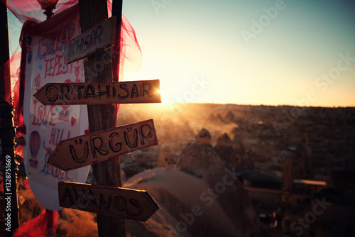 Signpost with names of villages and towns in Cappadocia opposite setting sun in Goreme sunset point, Nevsehir province, Turkiye