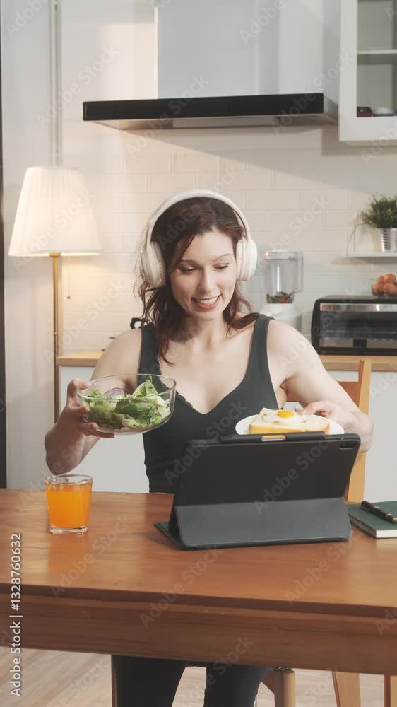 A white woman joyfully prepares a fresh salad in her kitchen, mixing lettuce, tomatoes, and cucumbers. She smiles while enjoying her meal during a video call with her boyfriend. A white woman joyfully prepares a fresh salad in her kitchen, mixing lettuce, tomatoes, and cucumbers. She smiles while enjoying her meal during a video call with her boyfriend.