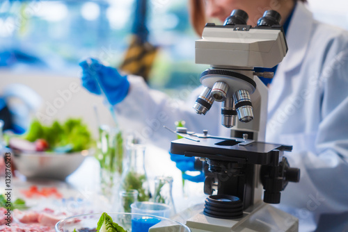 Wallpaper Mural Middle-aged female laboratory worker wearing blue gloves conducts lab test on food ingredients lettuce, cucumber, pork. Using microscope, she analyzes nutrients, preservatives, food safety records. Torontodigital.ca