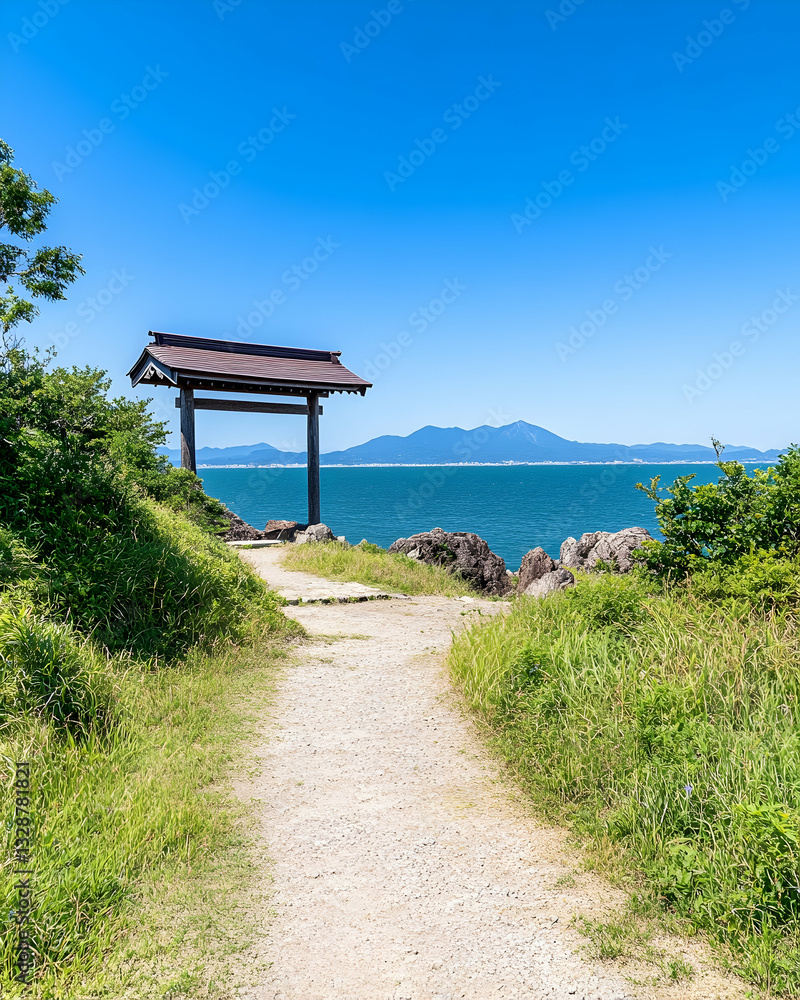 Coastal pathway leads to a wooden torii gate overlooking a calm sea and distant mountains under a clear blue sky Coastal pathway leads to a wooden torii gate overlooking a calm sea and distant mountains under a clear blue sky
